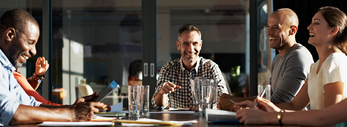 Colleagues laughing at a boardroom meeting table